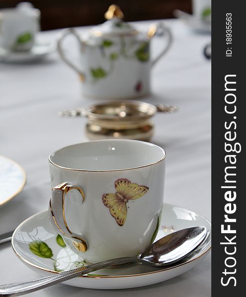 A teacup and saucer with spoon are in the foreground with other pieces in the background. A teacup and saucer with spoon are in the foreground with other pieces in the background.
