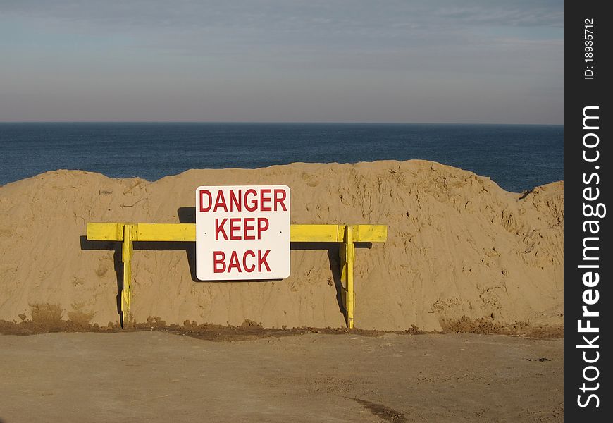 This is a photo of  a danger sign in front of a sand pile in front of eroding beach. This is a photo of  a danger sign in front of a sand pile in front of eroding beach