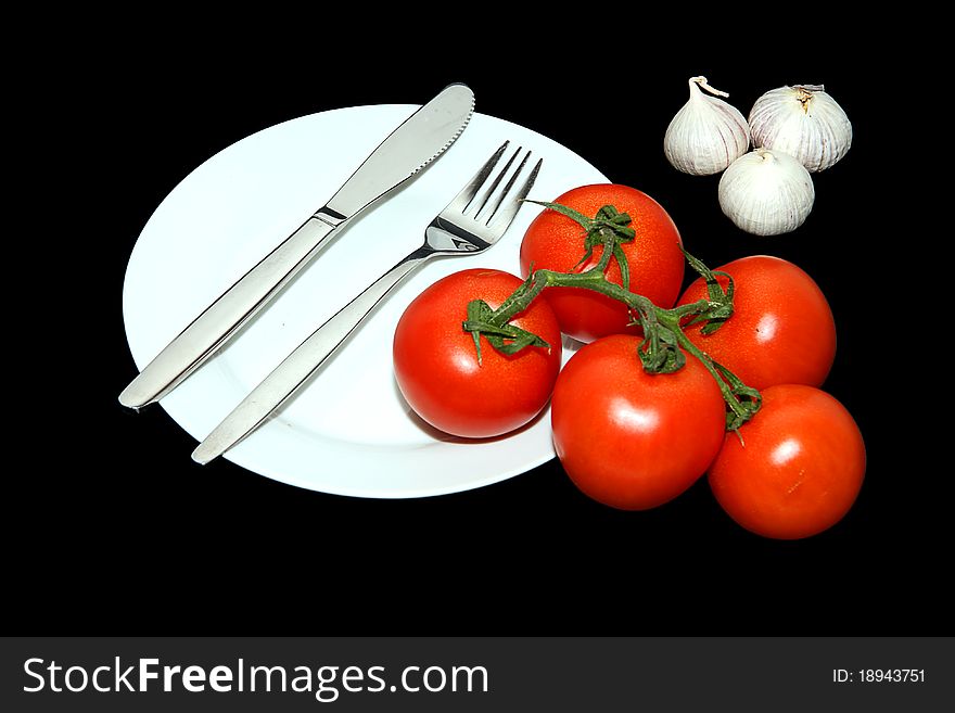 A Knife and Fork on a plate with tomato and garlic arranged. A Knife and Fork on a plate with tomato and garlic arranged