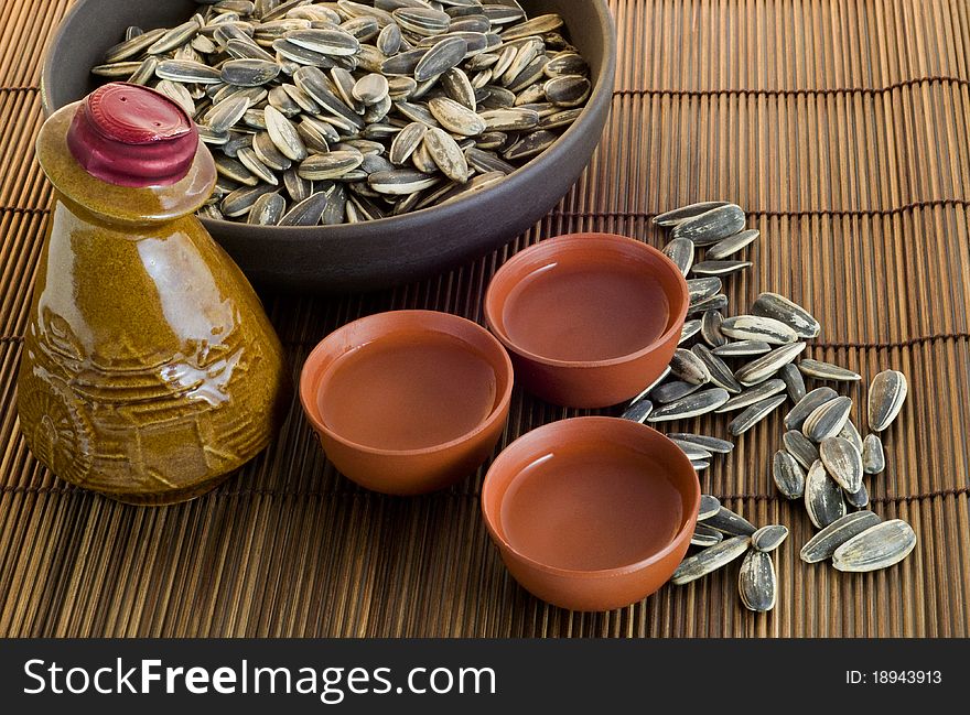 Chinese antique wine bottle with wine cups and sunflower seeds on brown bamboo table mat. Chinese antique wine bottle with wine cups and sunflower seeds on brown bamboo table mat.