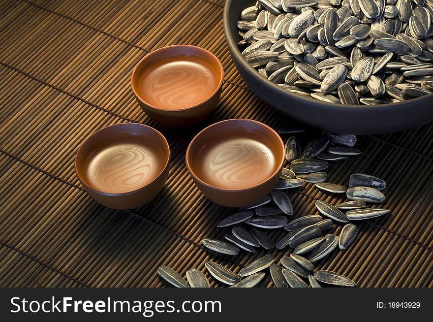 Sunflower seeds and three Asian clay tea cups on bamboo table mat. Sunflower seeds and three Asian clay tea cups on bamboo table mat.