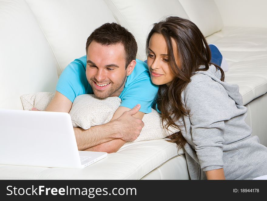 Young couple with laptop lying on the sofa at home