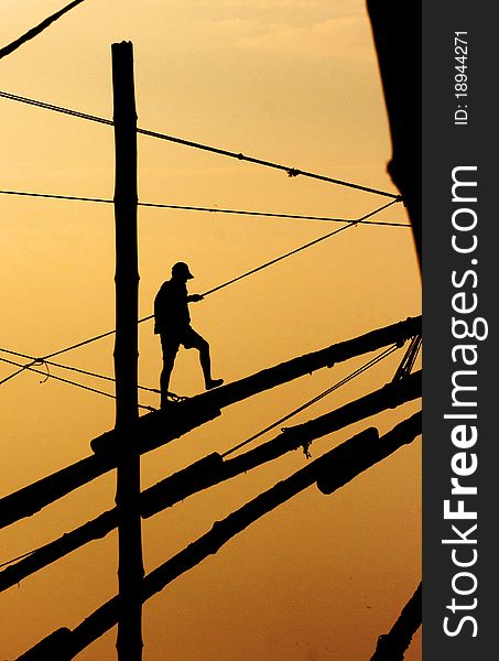 Fisherman walking on a mast in the sunset
