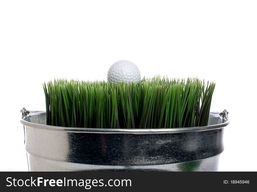 Horizontal image of a golf ball on grass in a small container on white. Container gardening