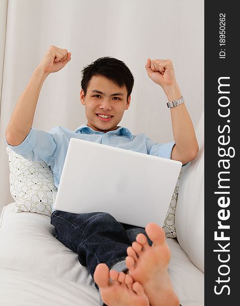 An excited man with arms upraised while using a laptop on a sofa. An excited man with arms upraised while using a laptop on a sofa