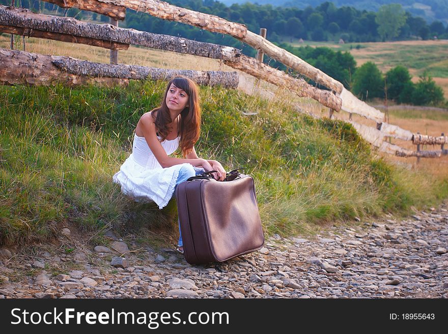 young girl in white dress, standing on the side of the country road on a luggage and waiting for a ride. young girl in white dress, standing on the side of the country road on a luggage and waiting for a ride.