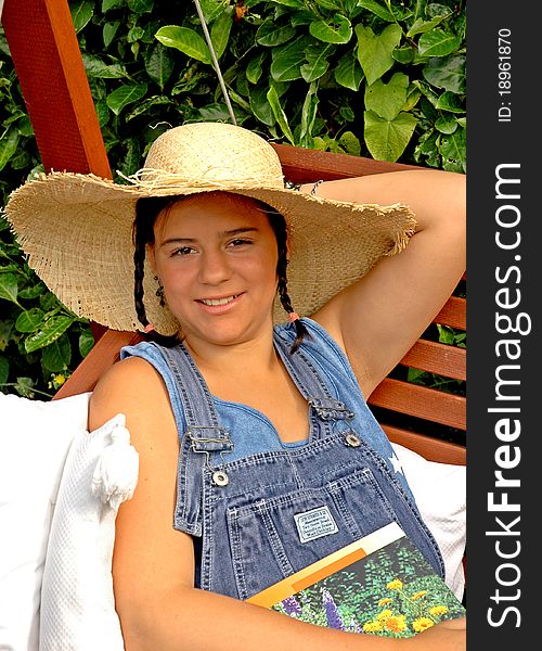 A young woman sitting in a garden swing, smiling and wearing a straw hat. A young woman sitting in a garden swing, smiling and wearing a straw hat