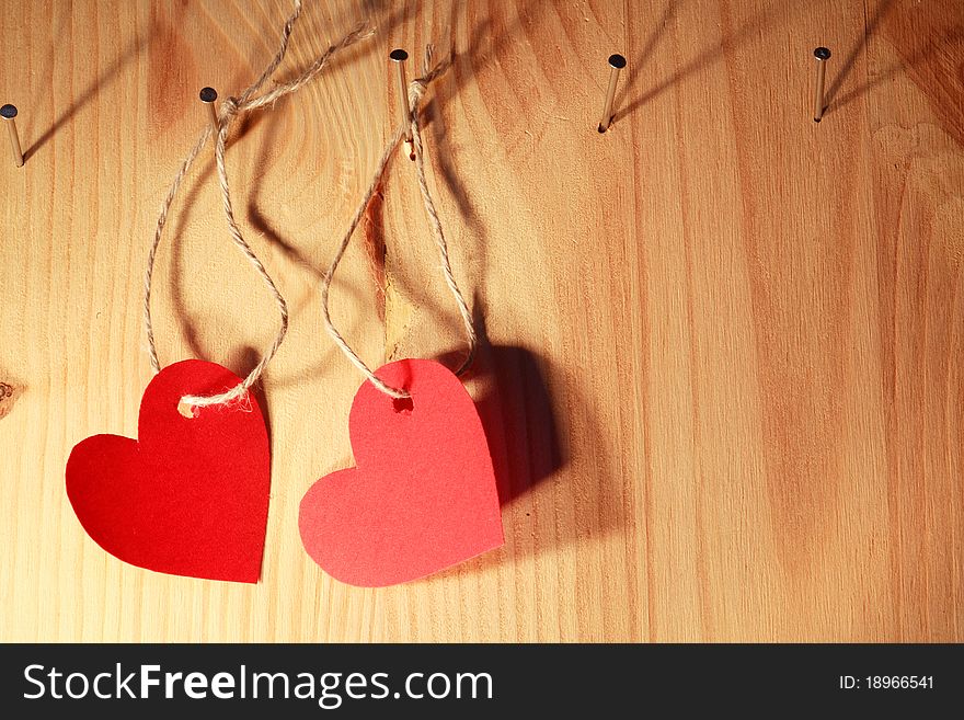 Two red paper hearts hanging on wooden wall with nails and ropes. Two red paper hearts hanging on wooden wall with nails and ropes