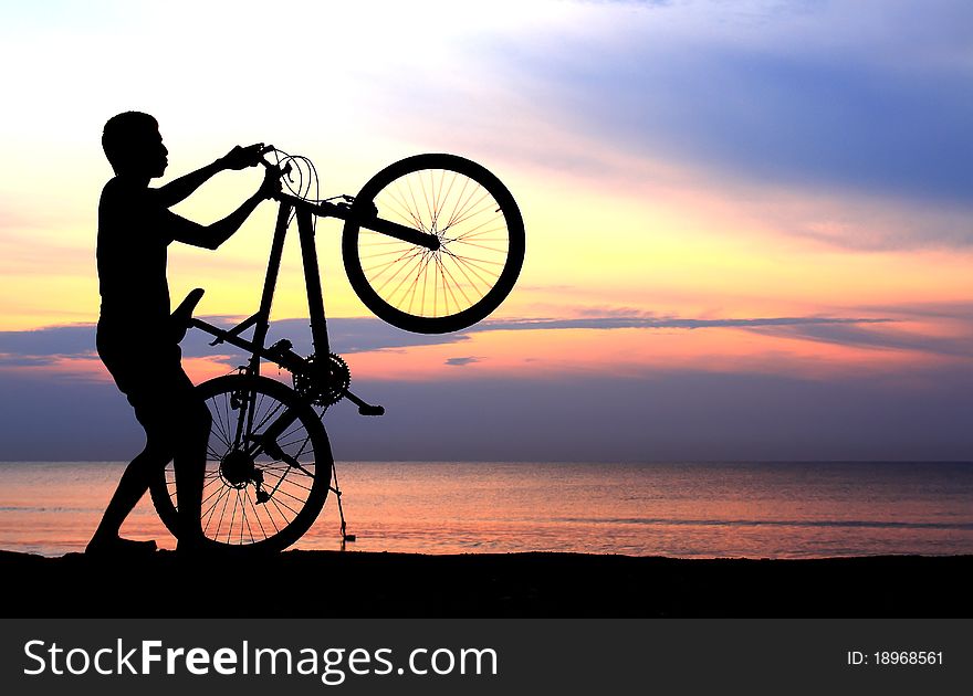 Silhouette of man riding bicycle with beautiful lake near by at sunset