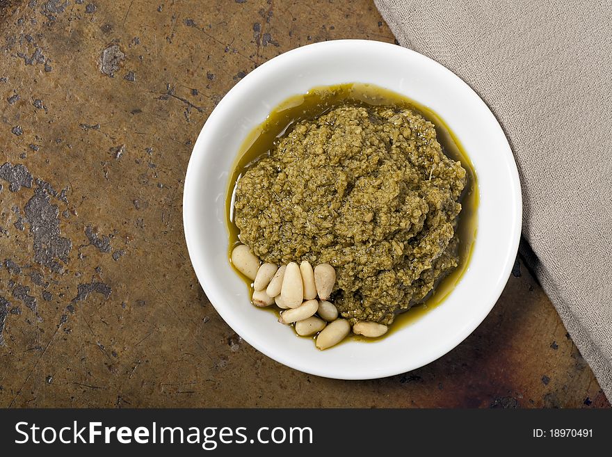 Fresh pesto in white bowl with pine nuts on a stone counter top.