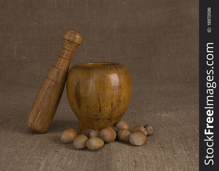 Wooden mortar and pestle with nuts on brown canvas