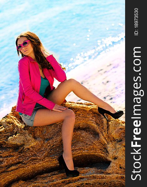 Girl sitting on a stone against a beach. Girl sitting on a stone against a beach