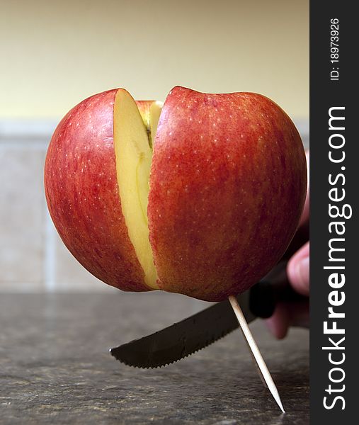 Red apple being cut in half with a sharp knife being held up by one single toothpick