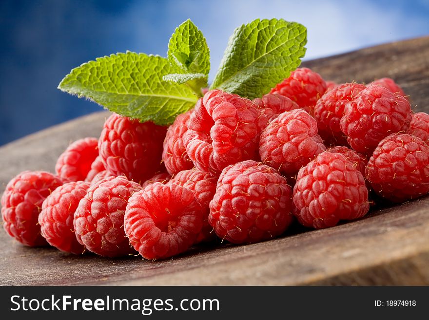 Photo of delicious red raspberries with mint leaves on wooden table
