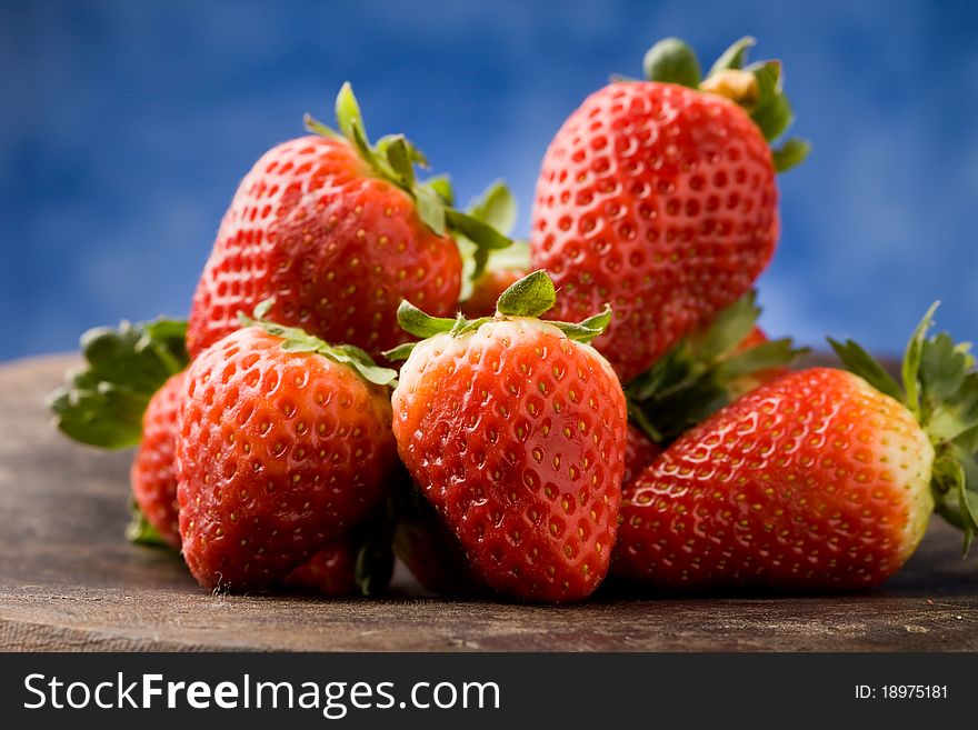 Photo of delicious red strawberries on wooden table in front of a blue background