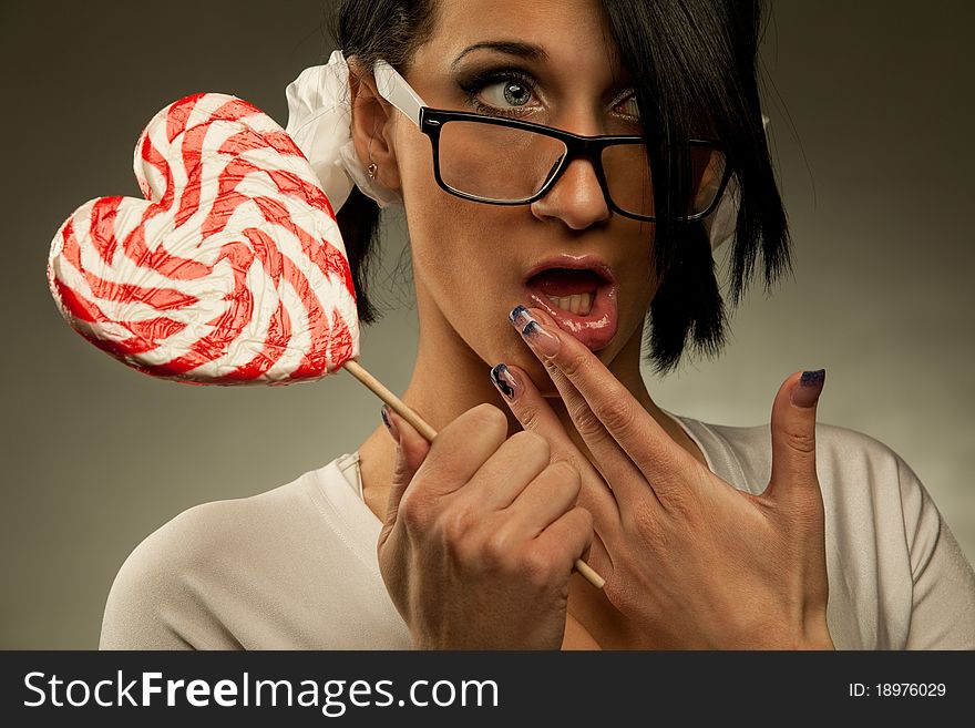 Funny woman with heart shaped lollipop licking her lips