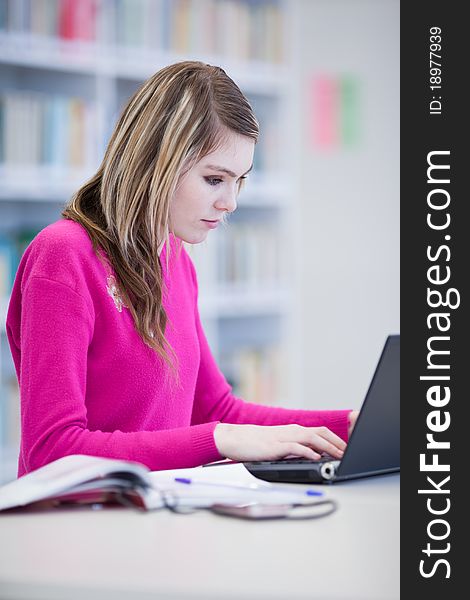 In the library - pretty, female student with laptop and books working in a high school library (color toned image)