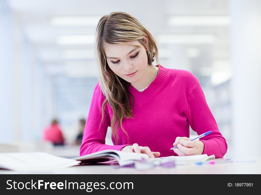 In the library - pretty, female student with laptop and books working in a high school library (color toned image)