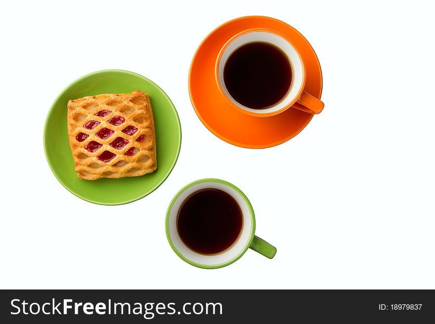 There are two cups with tea on the white background, orange and green. Also there are sweets on the saucer