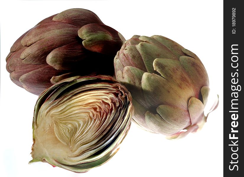 Three artichokes in group, one sliced, isolated on white background