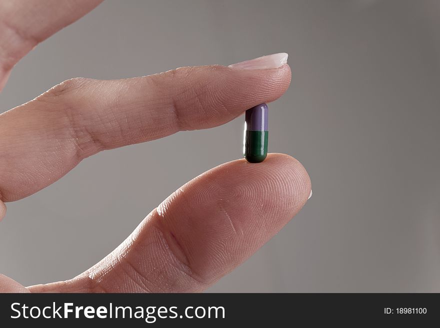 Female hand holding pill, isolated on gray. Female hand holding pill, isolated on gray
