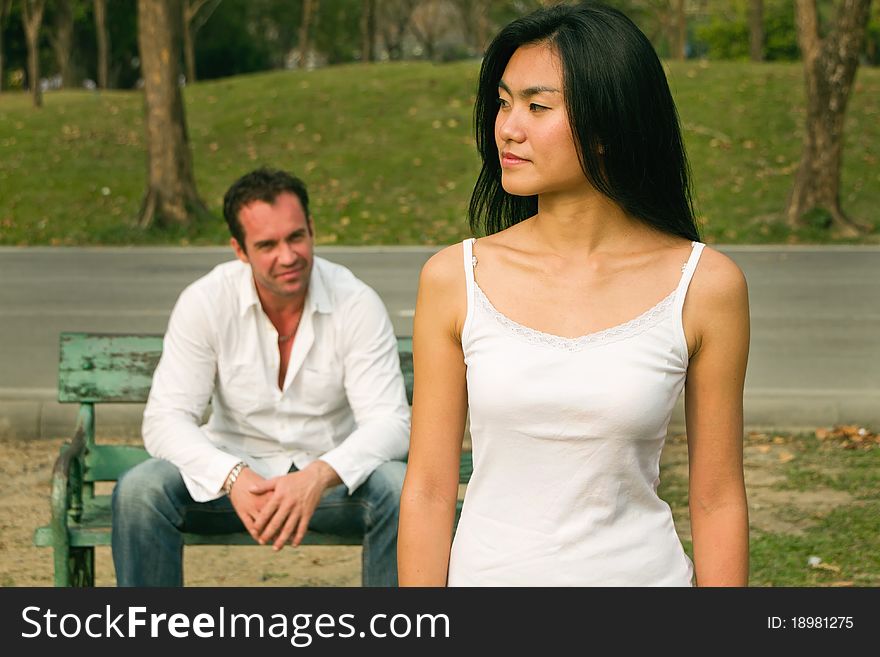 Woman do not look happy standing in front of man sit on chair