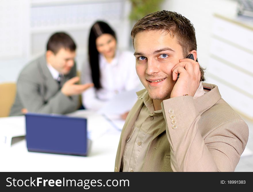 Young smiling businessman calling on phone at office