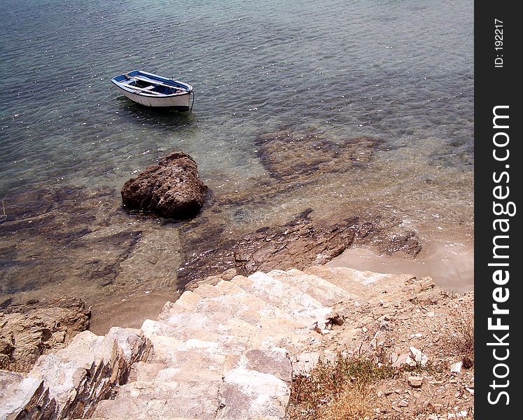 Stone tile steps leading to the shore with an old row boat in the greek islands