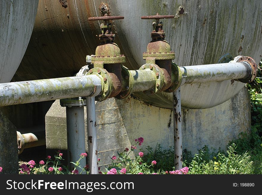 This is a picture of some old and in parts rusting pipes in front of a large tank. This is a picture of some old and in parts rusting pipes in front of a large tank.