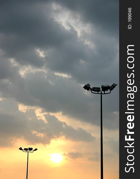 A pair of flood lighting poles sillouetted against the setting sun under some stormy clouds. A pair of flood lighting poles sillouetted against the setting sun under some stormy clouds