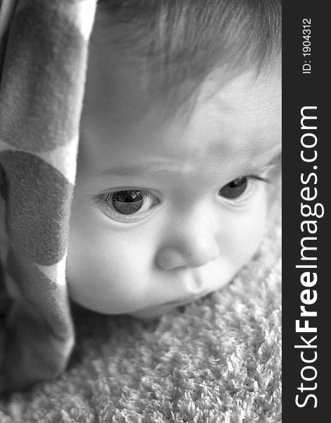 Black and white image of baby peeking out from under a blanket. Black and white image of baby peeking out from under a blanket