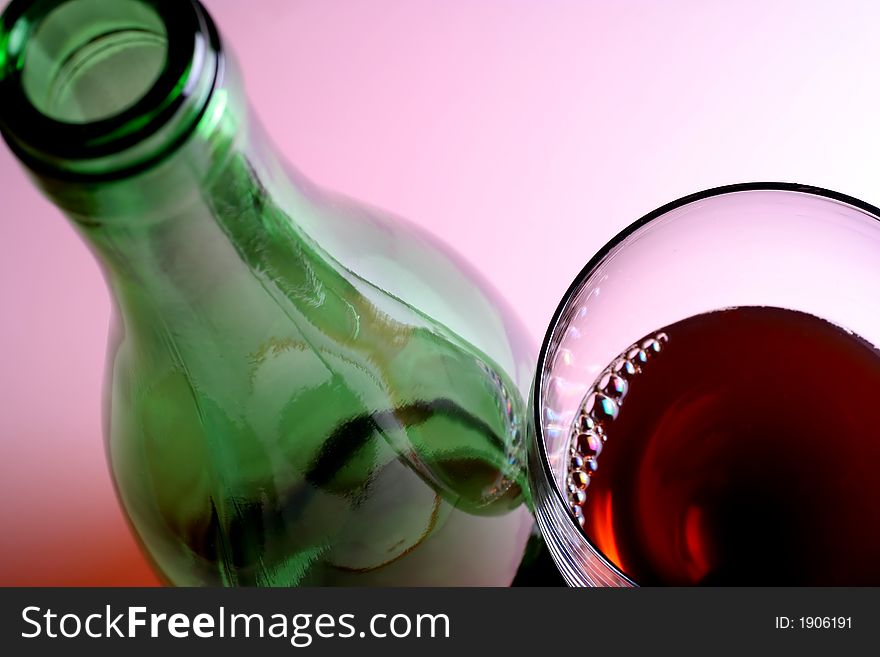 Green wine bottle and glass of red wine against pinkish white background. Green wine bottle and glass of red wine against pinkish white background.