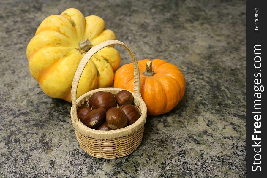 A basket of chestnuts, a yellow Carnival squash and a miniature pumpkin are autumn havest. A basket of chestnuts, a yellow Carnival squash and a miniature pumpkin are autumn havest.