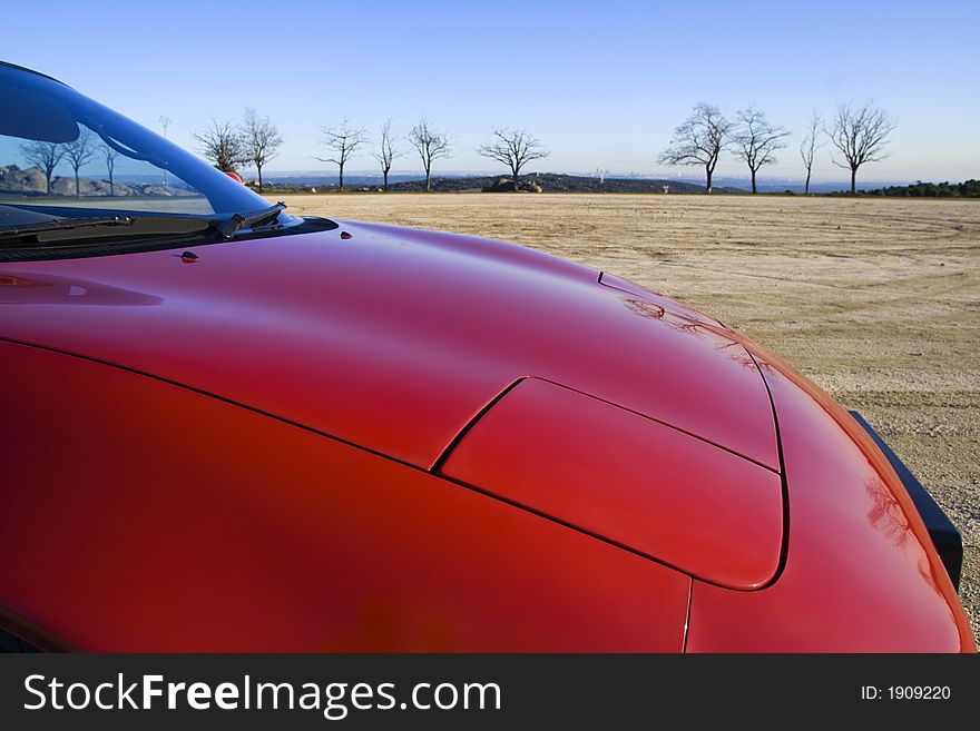 Nose of a classic red sports car on a dust track with perfect blue sky. Nose of a classic red sports car on a dust track with perfect blue sky.