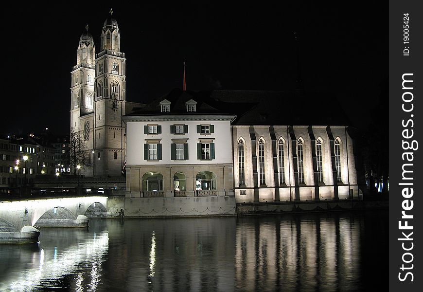 Night photo of Zurich cathedrale on the lake. Many lights creating great reflections of cathedrale and bridge.