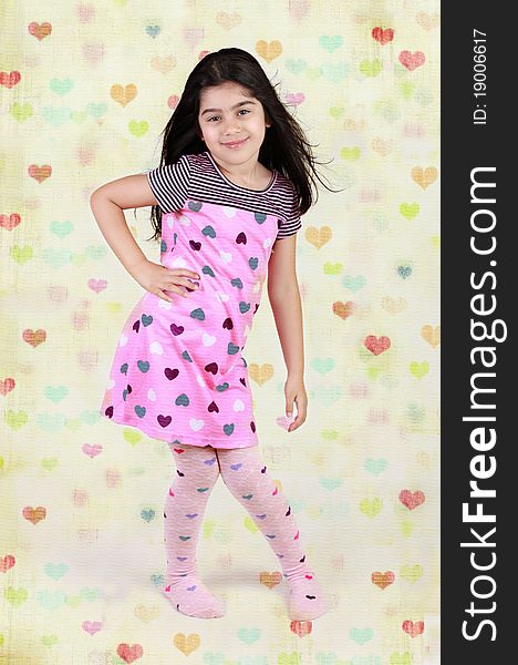 Little girl dressed in heart shaped dress and leggings with hears background. Little girl dressed in heart shaped dress and leggings with hears background.