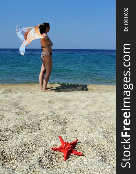 Blury attractive female on beach with focused red sea star on sand