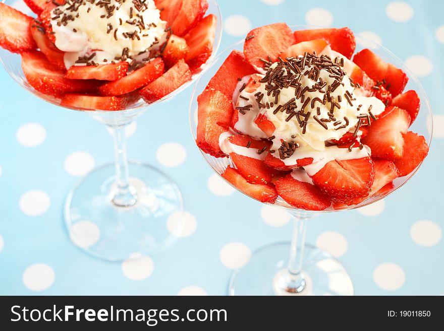 Sliced fresh strawberries and cream in martini glasses on blue polka dot background. Sliced fresh strawberries and cream in martini glasses on blue polka dot background