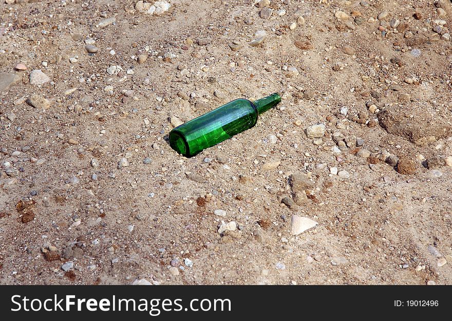 Lone green empty bottle left in the sand. Lone green empty bottle left in the sand