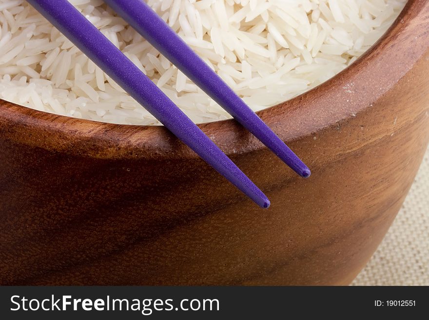 Close-up of white rice in a brown plate and purple chopsticks.