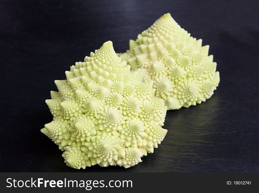 A pair of pale green baby cavolo romanesco on a slate surface