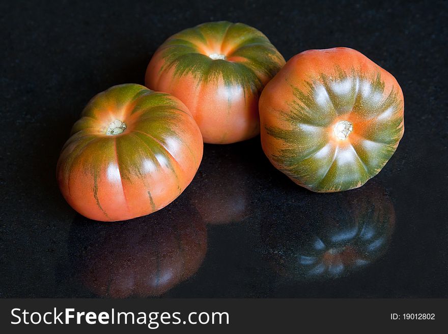 Three red marmonde tomatoes with distinctive green stripes against a black granite background