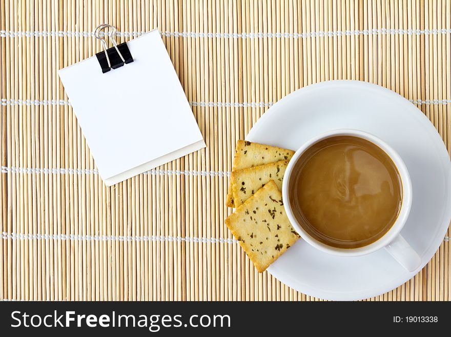 Cup of hot coffee and white sketch book on a mat