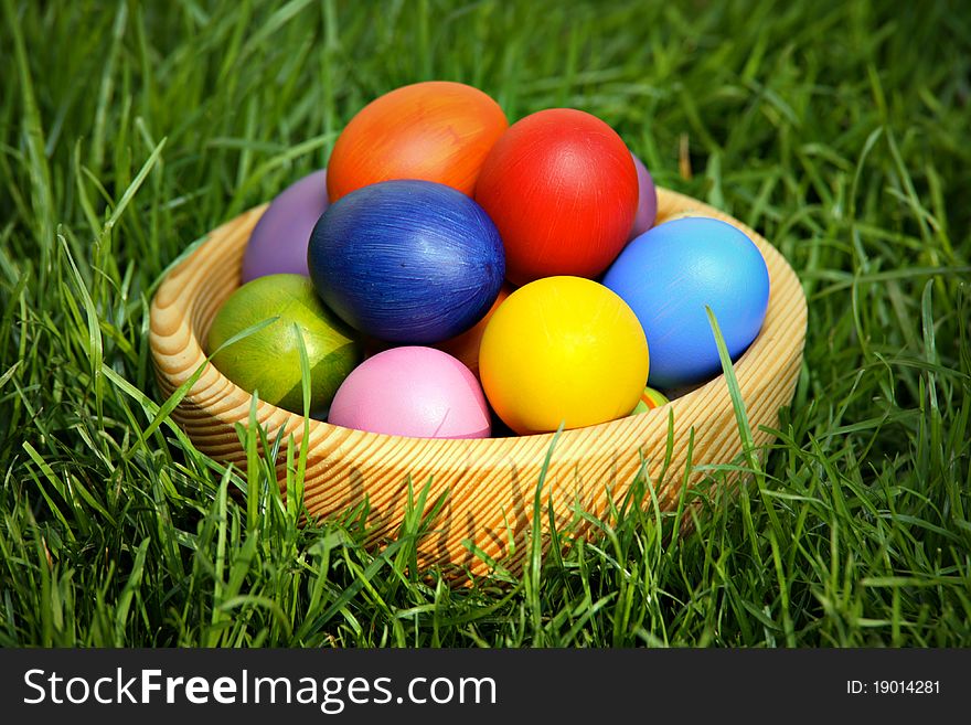 Colorful Easter eggs in wooden bowl, hidden in the grass
