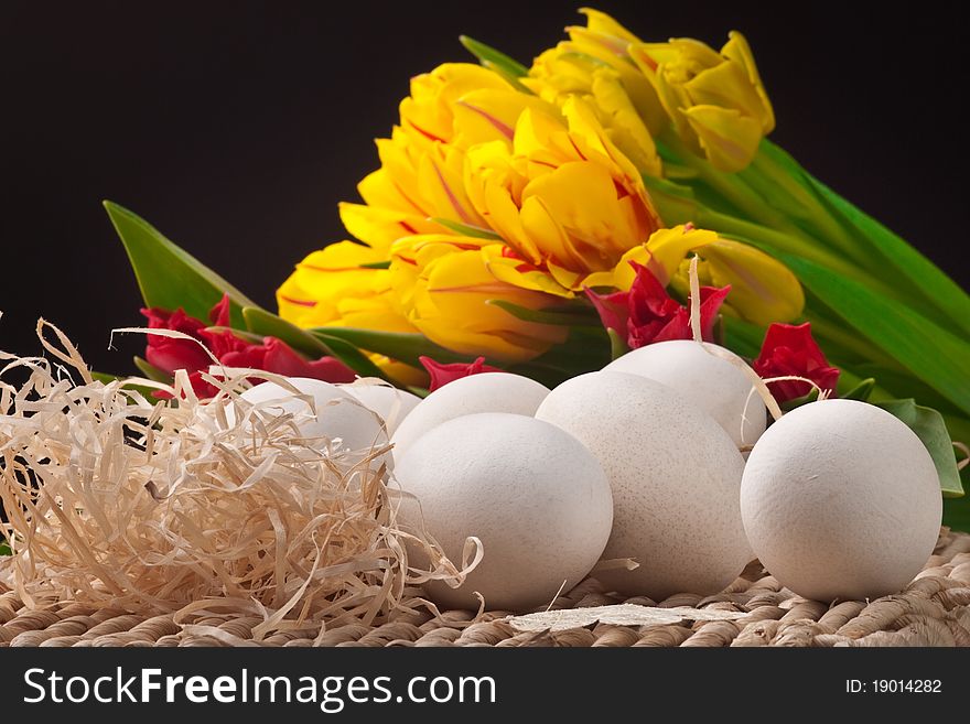 Yellow and red tulips with white eggs on straw tray