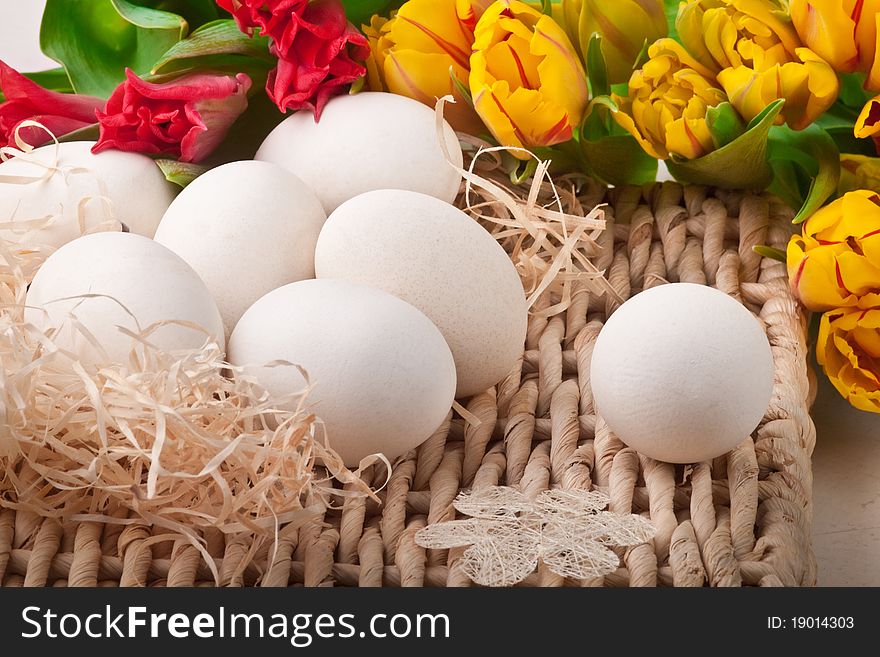 Seven white eggs and flowers lying on straw tray