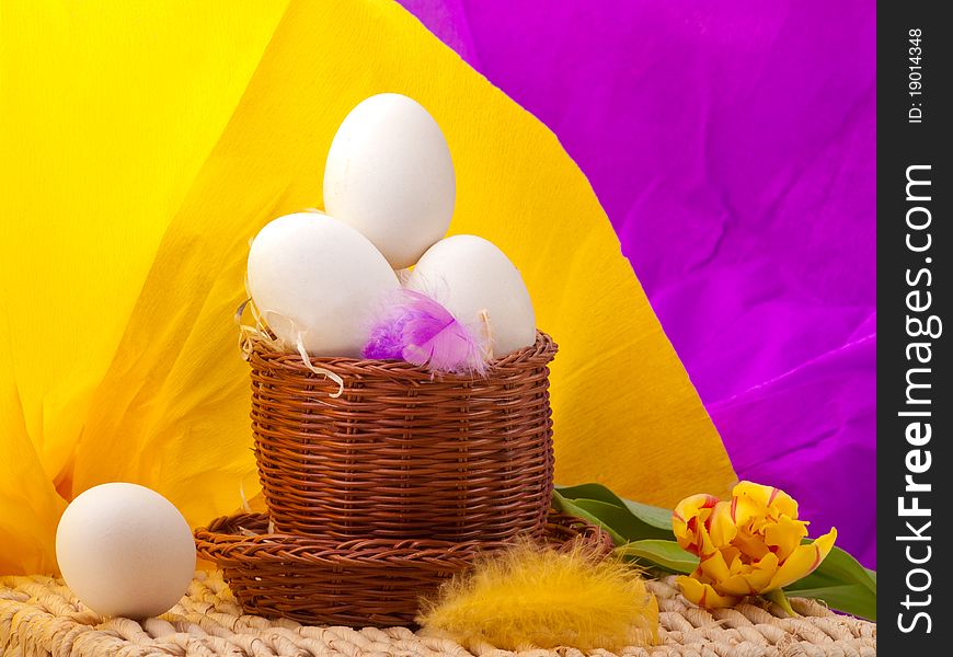 Eggs in straw basket with yellow and purple background on tray