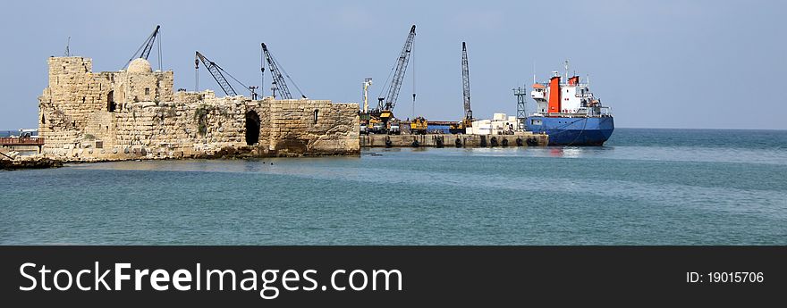 Tower cranes and boats in back of an ancient sea castle. Tower cranes and boats in back of an ancient sea castle