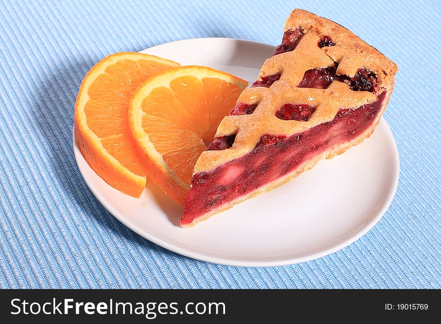 Cherry pie piece in a dish with two slices of orange. Cherry pie piece in a dish with two slices of orange.