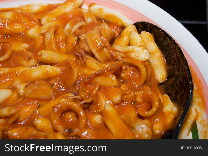 Cavatelli with an Italian Calamari Sauce in a serving dish on a black tile table. Cavatelli with an Italian Calamari Sauce in a serving dish on a black tile table.